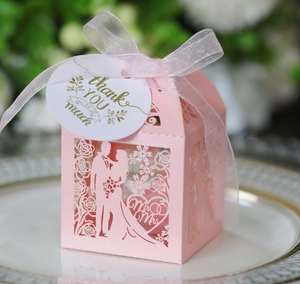 Macro shot of laser-cut Mr & Mrs candy box with pink ribbon on a gold-rimmed porcelain plate