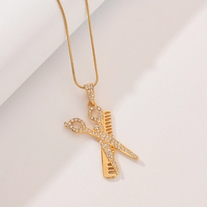 Close-up of gold scissors and comb pendant with sparkling crystals on a snake chain