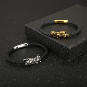 Close-up of braided leather bracelets with gold and silver dragon heads on black texture
