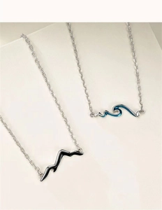 Close-up of mountain and wave pendants on silver chains for couples' jewelry set