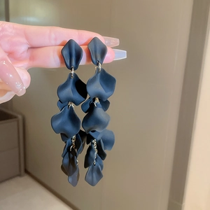 Macro detail of elegant black petal tassel earrings with gold link accents and matte finish