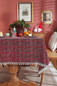 Close-up of red plaid Christmas tablecloth with white snowflake patterns and ball fringe