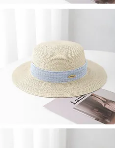 Detailed macro view of straw hat with light blue textured ribbon and golden oval metal logo