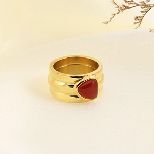 Close-up of gold wavy band ring with a triangle red stone inlay on a neutral background