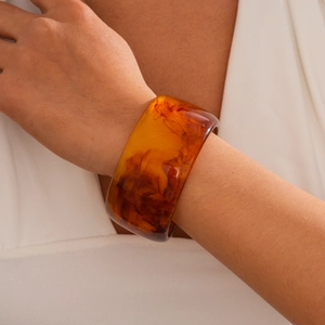 Close-up of wide amber resin bangle with tortoiseshell texture worn on a model's wrist