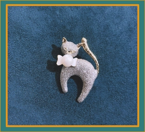 Detailed view of a stylized cat brooch with textured silver metal and a pearl accent