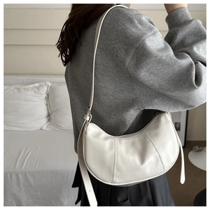Detail view of white leather crescent moon bag with silver buckle worn as an underarm purse