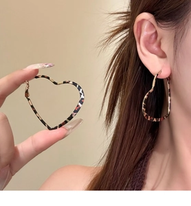 Detail of large heart-shaped earrings with leopard print pattern worn by a model