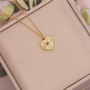 Close-up of golden hammered heart necklace with blue zircon on beige jewelry box
