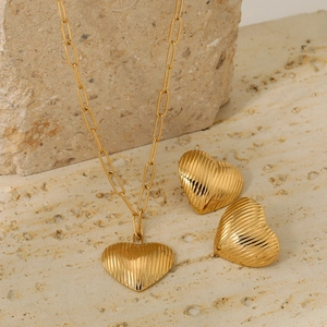 Golden heart jewelry set with vertical stripes, necklace and stud earrings on stone