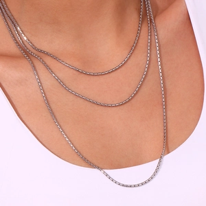 Close-up of three layered silver box chain necklaces worn by a model for a chic look