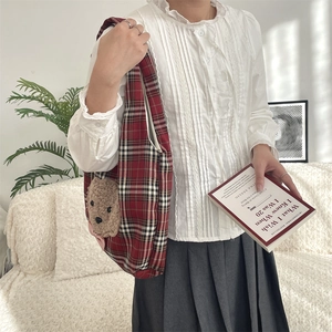 Detail of red plaid tote bag with plush bear head and bow on cozy home background