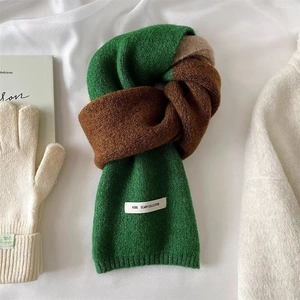 Gros plan d'une écharpe en tricot vert et marron avec étiquette et gants blanc crème