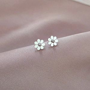 Macro shot of silver daisy earrings resting on pink silk fabric showing petal details