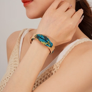Detail of floral fabric and gold metal bead bracelet worn on wrist by female model