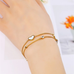 Detail of double-layer gold heart bracelet with clear gemstones on model wrist