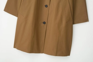 Detail view of khaki trench coat featuring resin buttons, side pockets and twill fabric