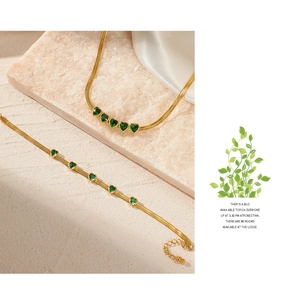 Detailed view of the gold snake chain necklace and bracelet set with green heart gems