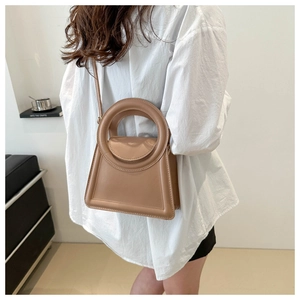 Minimalist light brown leather tote bag with unique circular handle and trapezoidal shape