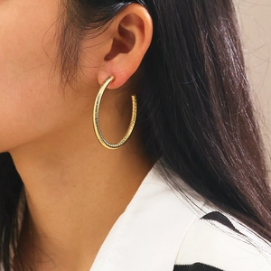 Close-up of model wearing large gold hoop earrings with spiral texture and glossy finish
