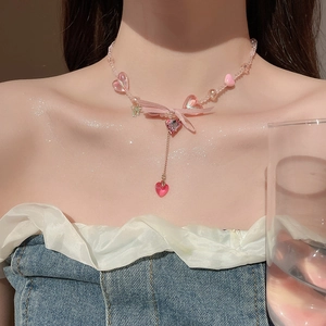 Close-up of pink beaded choker necklace with ribbon bow and heart pendants on collarbone
