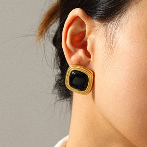 Close-up of vintage square black stone earring with golden textured frame on model's ear