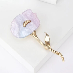 Detailed close-up of a pink floral brooch with golden metal leaves on a white stand