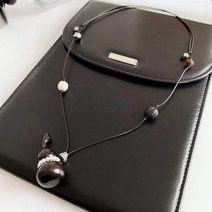 Detail of wooden gourd pendant necklace with white pearls on a black leather clutch