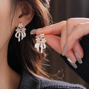 Détail de boucles d'oreilles fleurs et nœuds dorées avec zircons sur modèle