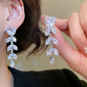 Close-up of long silver drop earrings with heart and leaf zircon crystals on a model