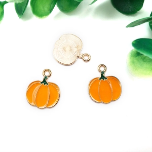 Detailed view of three gold pumpkin charms with orange enamel and shiny textured backs