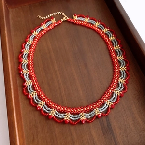 Detail of red and gold handcrafted beaded necklace with intricate wave pattern on wood