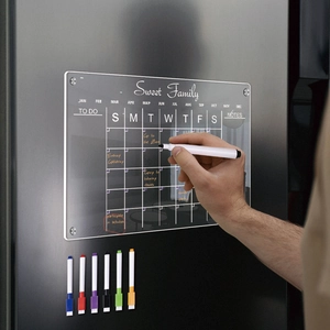 Close-up of hand writing on a magnetic acrylic monthly planner with colorful markers