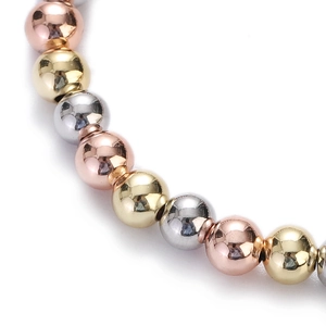 Macro detail of polished gold, rose gold, and silver beads in a three-color metal bracelet