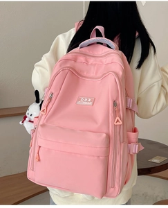 Rear view of a pink multi-pocket nylon backpack with side buckles and white charm