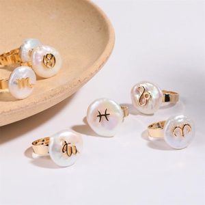Baroque pearl rings with golden zodiac signs and irregular shapes on white ceramic