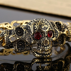 Vintage gold skull bracelet with red crystal eyes on a reflective black surface