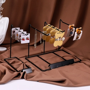 Two black metal desktop jewelry stands for earrings and necklaces on brown fabric