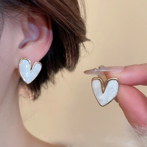 Detailed view of heart-shaped gold-framed stud earrings with elegant white resin inlay