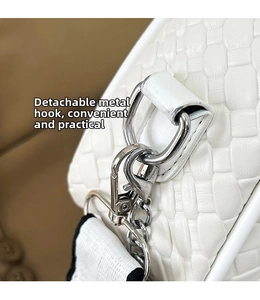 Close-up of white woven shoulder bag featuring silver metal hooks and detachable strap