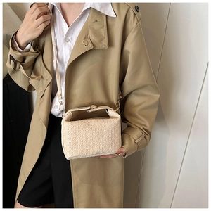 Close-up of beige woven texture handbag with gold hardware styled with a trench coat