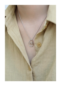 Close-up of minimalist silver irregular heart pendant worn on a cotton linen shirt