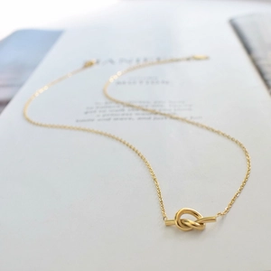 Macro detail of a golden knot pendant on a minimalist stainless steel chain necklace