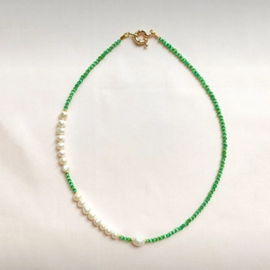 Detail of beaded necklace featuring green cat eye stones and white baroque pearls
