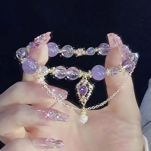 Detail of purple beaded bracelet with gold accents and a droplet gemstone charm