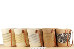 Detail of five woven straw bucket bags with brown leather straps on wood surface