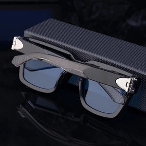 Detail of square black frame sunglasses with silver metal hinge on a textured black box