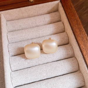 Macro detail of matte pearl square earrings on a beige fabric jewelry box cushion