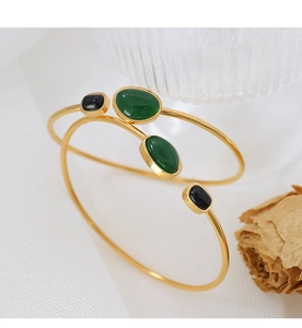 Detail view of gold open bangles featuring black onyx and dark green oval gemstones
