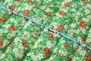 Detail of green floral quilted fabric with colorful print and blue piping edge finish